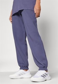 Pantalons de jogging violets avec une taille élastique et des manchons, associés à des chaussures de sport blanches avec des accents gris et une semelle texturée.