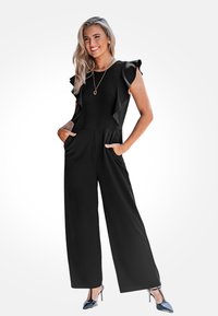 Jumpsuit nero con maniche a volant, design a gamba larga e tasche frontali. Texture liscia con bustino aderente, abbinato a tacchi alti lucidi.