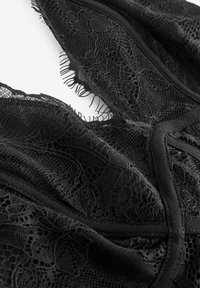 Tela de encaje negra con intrincados patrones florales, con bordes sin acabado y forro suave. Textura suave y costuras detalladas visibles.