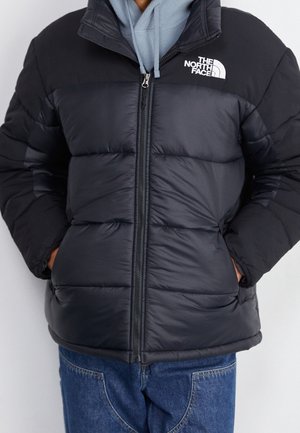 Personne portant une doudoune noire North Face par-dessus un sweat à capuche bleu clair et un jean bleu, les mains dans les poches de la veste.