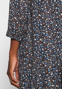 Floral-patterned fabric in dark blue with small white and colorful flowers. Features a loose fit and three-quarter length sleeves.