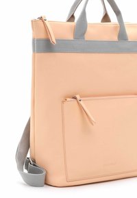 Peachfarvet tote bag lavet af glat materiale med grå stropper, enkelt lynlåslomme og en struktureret design. Bemærkelsesværdigt logo nederst.