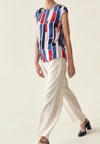 Femme marchant vêtue d'un haut sans manches à rayures multicolores, de pantalons larges blancs et de chaussures à talons hauts noires.