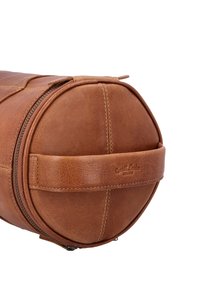 Hnedá kožená valcová taška s horným zipsom, pevnou rukoväťou na prenášanie a jemnými detailmi šitia. Na boku vyrazené logo značky.