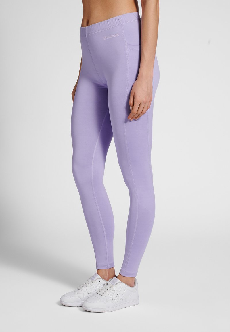 Ljuslila leggings med en mjuk textur, hög midja och sömdetaljer. Kombinerade med vita träningsskor.