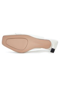 Chaussure blanche à talon haut avec un bout carré, semelle beige visible et talon bloc noir court vue du dessous.