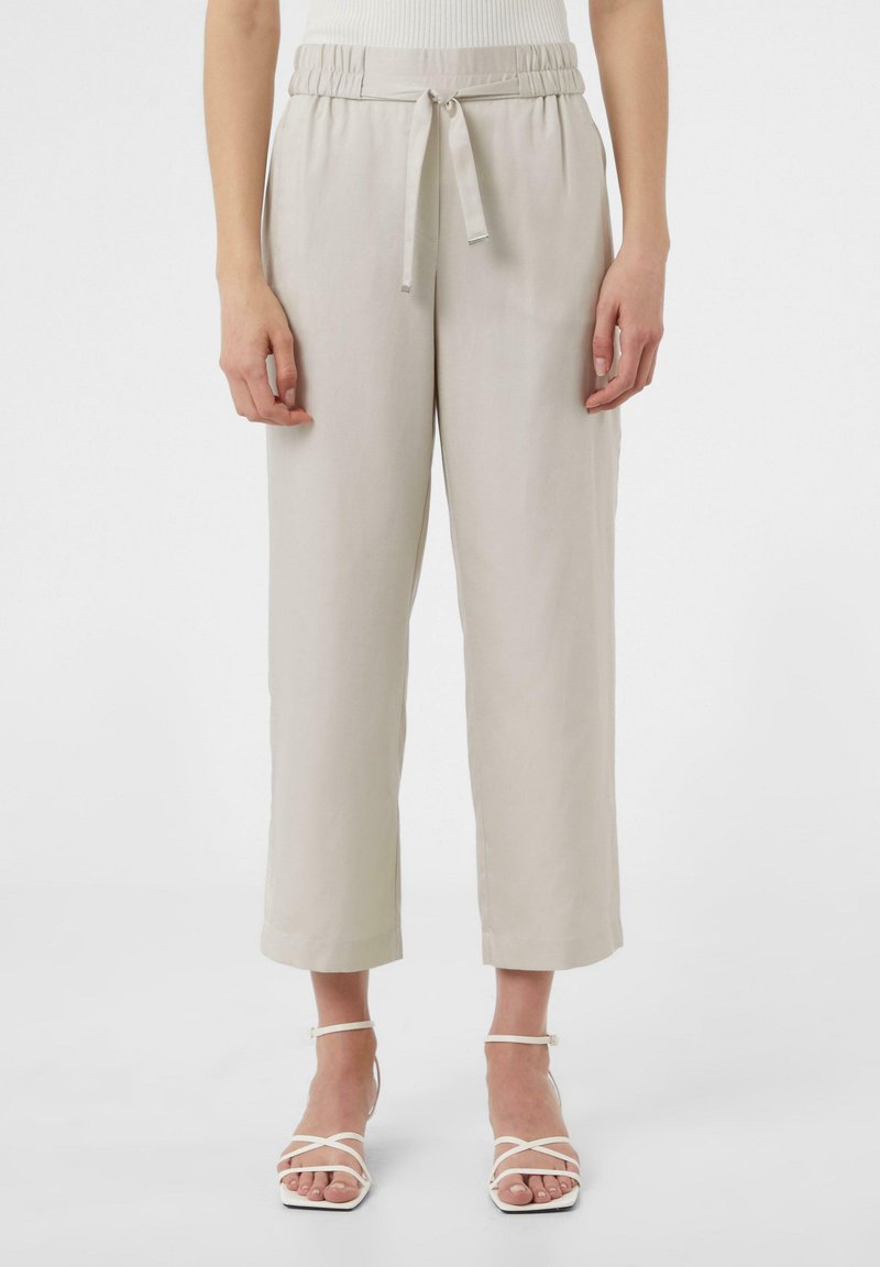 Jasno beżowe, luźne spodnie z pasem na sznurku, szerokimi nogawkami i gładką fakturą. Połączone z białymi sandałami na paski.