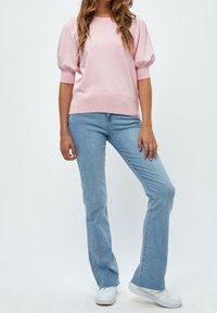 Helles rosa Strickoberteil mit kurzen, puffärmel, kombiniert mit hellblauen Schlagjeans. Weiße Sneaker runden das Outfit ab.