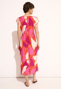 Sukienka maxi w odważnym wzorze różowych, czerwonych i białych abstrakcyjnych kształtów. Posiada krótkie rękawy, ściągniętą talię i luźny krój.