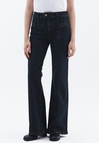 Tmavě modré zvonové džíny vyrobené z denimu, s předními kapsami, jemným prošíváním a vysokým pasem.