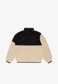 Beige faux-furjakke med svart nylonoverdel, høy krage, elastiske mansjetter og en kontrasterende svart horisontal stripe over skuldrene.