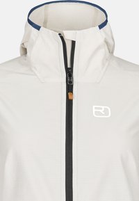 Light grey jacket with a high collar, black zipper, and a small white logo on the front. Features textured fabric with a subtle pattern.