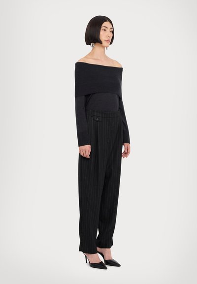 Haut noir à épaules dénudées avec texture côtelée, associé à un pantalon à rayures et taille haute et des chaussures à talons aiguilles noires.