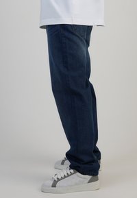 Jeans de mezclilla azul oscuro con un corte relajado, que presentan detalles de costura sutiles. Combinados con tenis blancos con acentos grises y paneles texturizados.