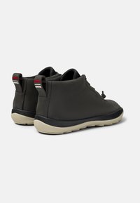 Botas de cuero gris hasta el tobillo con una textura suave, suela de goma negra y tiradores con un logo rojo y gris en la parte posterior.