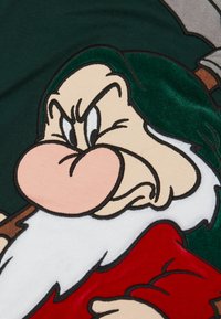Zelená tkanina s postavou trpaslíka v kresleném stylu, se výrazným nosem, bílým plnovouskem, červeným kabátem a vážným výrazem obličeje. Viditelné výšivkové detaily.
