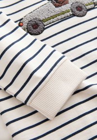 Chemise à manches longues avec des rayures horizontales bleu marine et des poignets côtelés, ornée d'un patch voiture texturé brodé sur la poitrine.