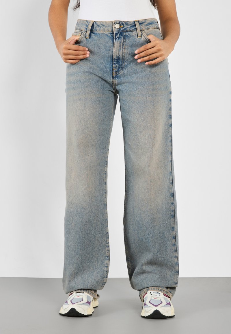 Ljust blå höga jeans med vida ben, tillverkade av denim. Har fem fickor och synlig sömnad längs sömmarna.