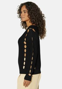 Schwarzer Pullover mit ausgeschnittenen, runden Designs an den Ärmeln, mit gestrickter Textur und gerippten Bündchen. Einfacher Rundhalsausschnitt und entspannte Passform.