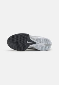 Nike treningssko med en svart strukturert gummisåle og en grå og hvit overdel, med en subtil logoaksecent og dynamisk design.
