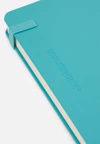 Quaderno Moleskine turchese con copertura testurizzata, chiusura con elastico e logo in rilievo. L'interno presenta pagine di colore crema.