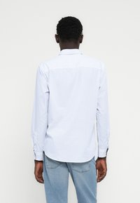 Λευκό πουκάμισο με μακριά μανίκια, μικρές ναυτικές μπλε πουά, κλασικό γιακά και κουμπιά στα μανίκια. Φορεμένο με ανοιχτόχρωμο μπλε τζιν.