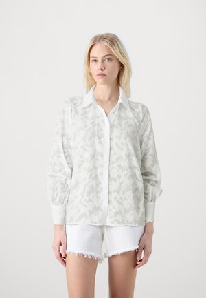 Chemise blanche à manches longues avec un motif floral subtil, avec un boutonnière à l'avant et un col. Associée à un short blanc effiloché.