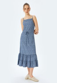 Blauwe jurk met bloemenprint, dunne straps, een aansluitend lijfje en een gerimpelde zoom. De stof lijkt lichtgewicht met een gladde textuur.