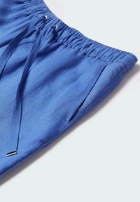 Pantalon bleu à taille élastique, poche latérale et cordons avec embouts métalliques sur fond clair.