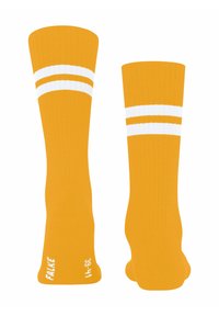 Une paire de chaussettes jaunes moutarde montantes jusqu'aux genoux avec deux rayures blanches près du haut et du texte blanc indiquant la taille et la marque sur la zone de la semelle.