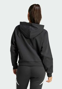 Černá mikina s kapucí, volného střihu, s žebrovanými manžetami a spodním lemováním. Má kontrastní bílé pruhy na ramenou a je vyrobena z měkkého materiálu.