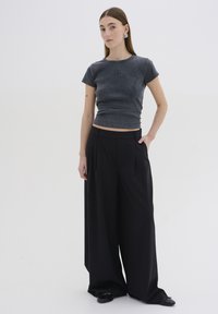 T-shirt grigio aderente in cotone con scollatura rotonda. Abbinato a pantaloni neri a vita alta e gamba larga. Scarpe nere basse.