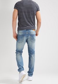 Blå denimjeans med slim fit, blekt tvätt, och bakfickor. Bärs tillsammans med en marinblå och vit randig t-shirt och vita sneakers.