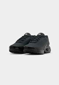 Black athletic shoes featuring a textured fabric upper, padded tongue, and a prominent black rubber sole with visible air cushioning.