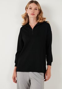 Černá mikina na zip s strukturovaným límcem, dlouhými rukávy a volným střihem. Vyrobena z měkkého materiálu s jemnou texturou.