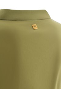 Olivgrüne Bluse mit glatter Textur, die einen kurzen Kragen hat und an der Rückseite mit einem kleinen rechteckigen Etikett mit Prägung versehen ist.