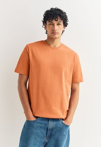 Orangenes T-Shirt mit kurzen Ärmeln aus einem weichen Stoff, mit Rundhalsausschnitt, kombiniert mit blauen Denim-Jeans. Einfaches Design mit entspannter Passform.