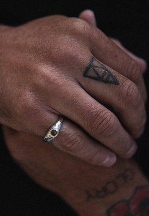 Silver ring with a round gemstone, featuring an organic design. Skin texture is visible, with a tattoo displayed on the hand.