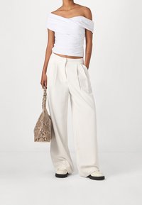 Top blanco de un solo hombro con pantalones plisados crema y un bolso de estampado de serpiente beige. Presenta un diseño de pierna ancha y zapatos gruesos blancos.