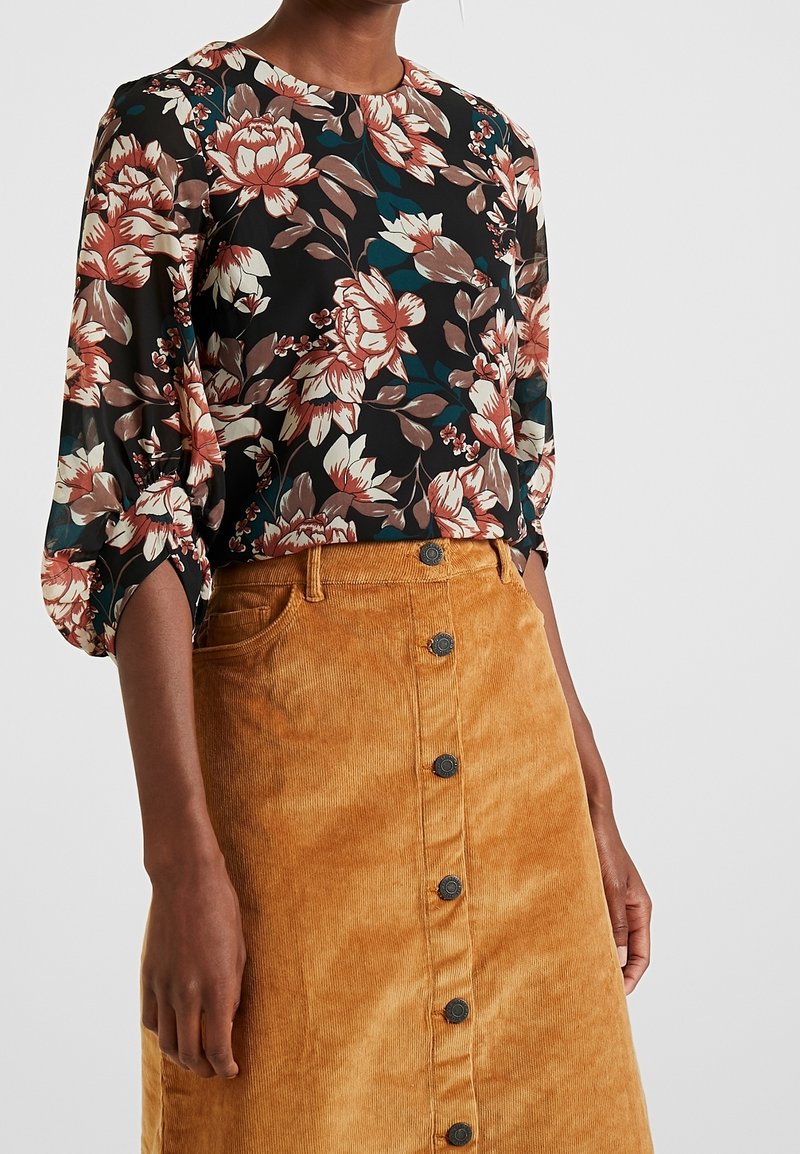 Bluzka z długim rękawem o czarnym tle i dużym kwiatowym wzorze w odcieniach kremu, brązu i morskim, połączona z spódnicą z taniego sztruksu.