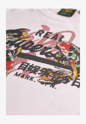 Camiseta blanca de algodón con un gráfico de dragón en strass multicolores y texto en negro y rojo, con cuello redondo y manga corta.