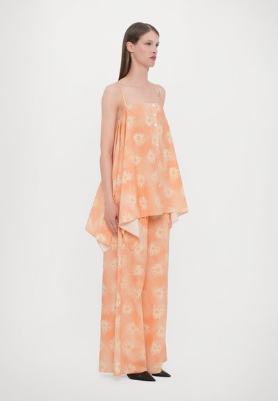 Perzikkleurige outfit met een vloeiende, mouwloze top met bloemmotieven en wijde broekspijpen. Gladde stof met een losse pasvorm.