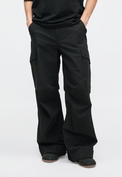 Juodi cargo kelnės laisvu siluetu, pagamintos iš lengvos medžiagos. Įrengtos šoninėmis kišenėmis, glotnia tekstūra ir plačių kojų dizainu.