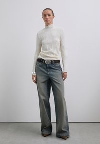 Crème coltrui met textuurstof, gecombineerd met lichtblauwe high-waisted wijde jeans en een zwarte riem met een ronde zilveren gesp.