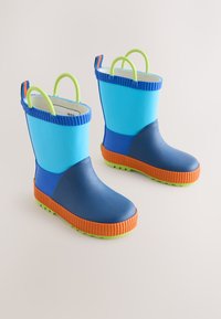 Bottes imperméables pour enfants avec tiges bleues, semelles orange et poignées vert citron sur un fond neutre.