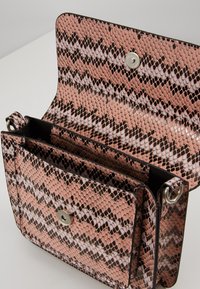 Borsa in finta pelle di serpente rosa con chiusura a calamita, dotata di un vano interno e rivestimento nero. Motivo rettile testurizzato.