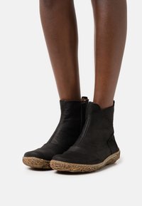 Černé kožené kotníkové boty se zipem, texturovaným svrškem a světle hnědou vzorovanou podrážkou. Mají minimalistický design a zaoblenou špičku.