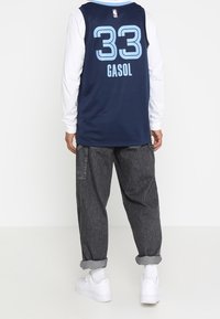 Maillot de basket-ball bleu marine avec manches longues blanches, comportant le numéro de joueur 33 en bleu clair et le nom "GASOL" dans le dos. Pantalons larges gris et chaussures blanches.