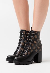 Černé kotníkové boty na robustním podpatku, s vzorovaným hnědým textilním designem, texturovanou černou kůží a kovovými očky.