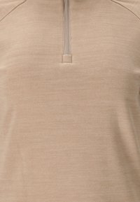 Beige kvart-zip fleece top med en kort lynlås og en lille stoftaw på kraven.
